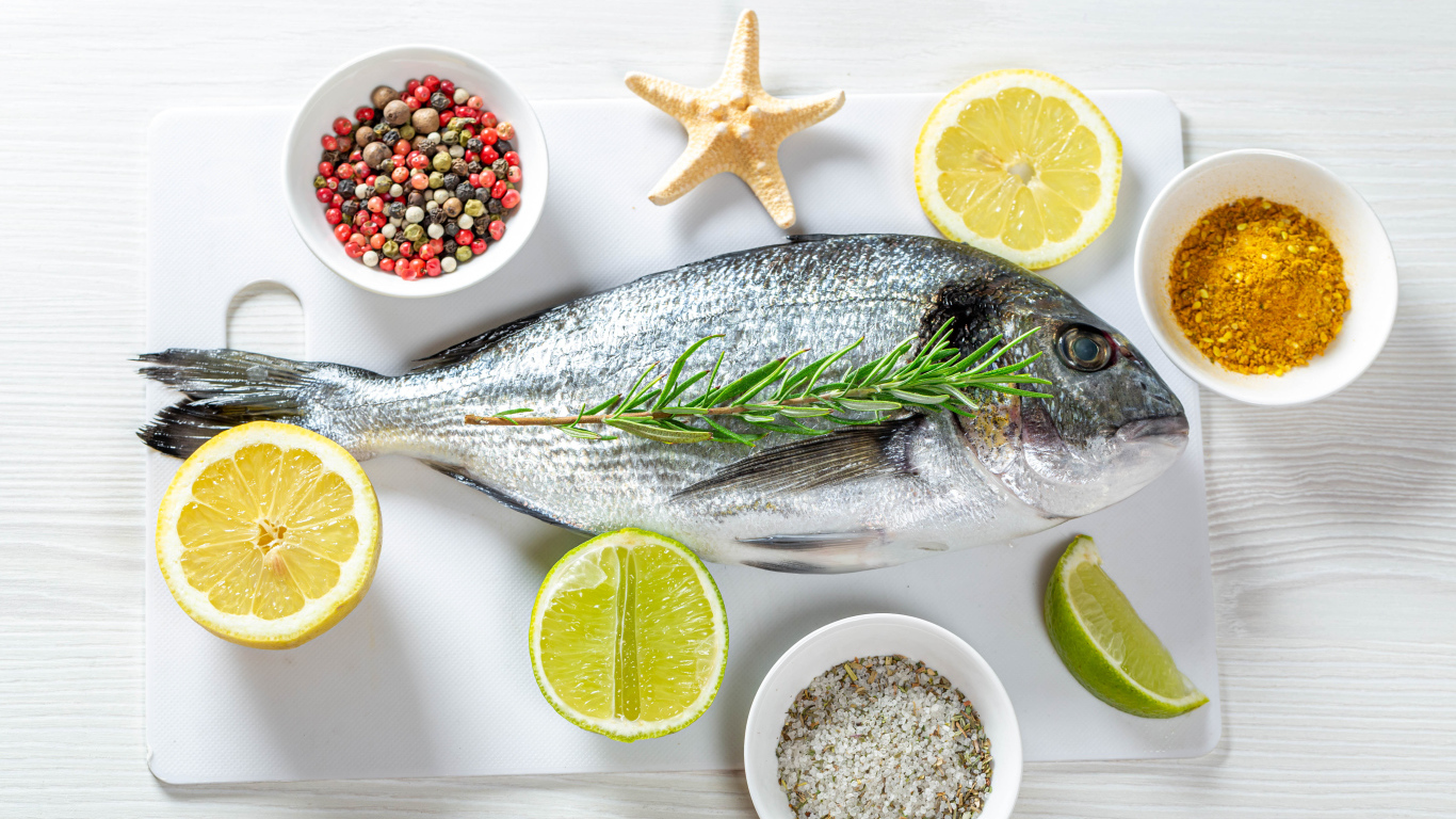 Свежая рыба на доске с солью, перцем, куркумой и лимоном