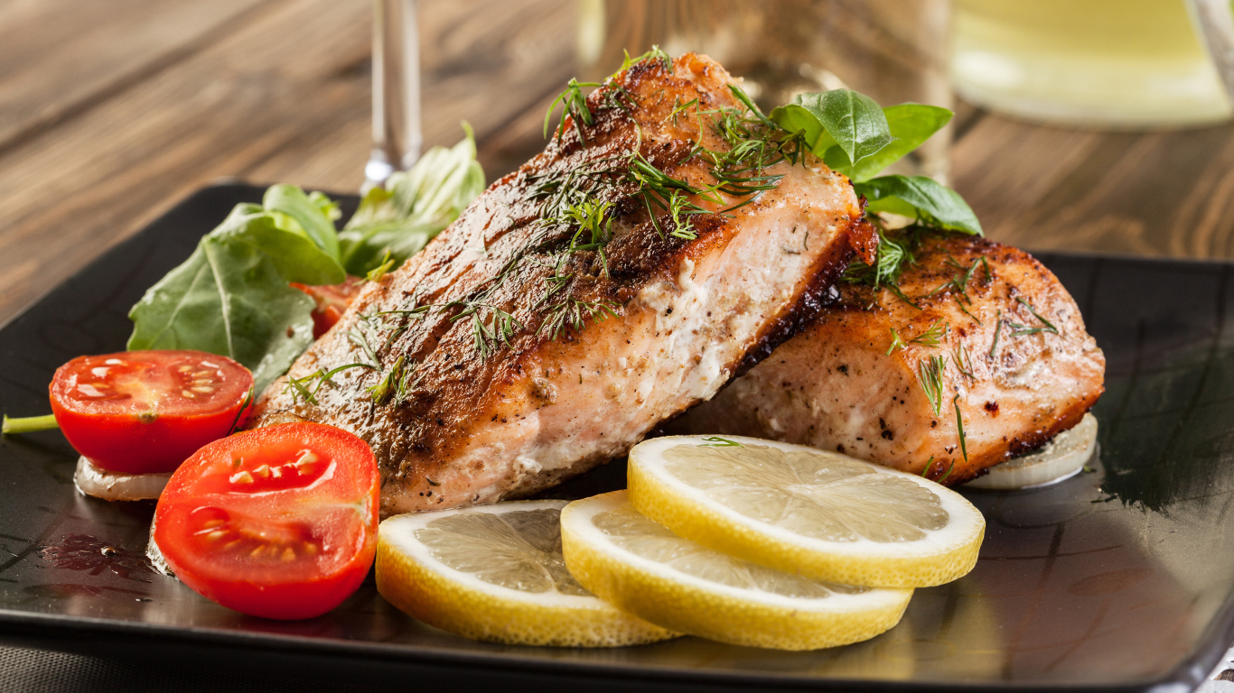 Куски запеченной рыбы на тарелке с помидорами и лимоном