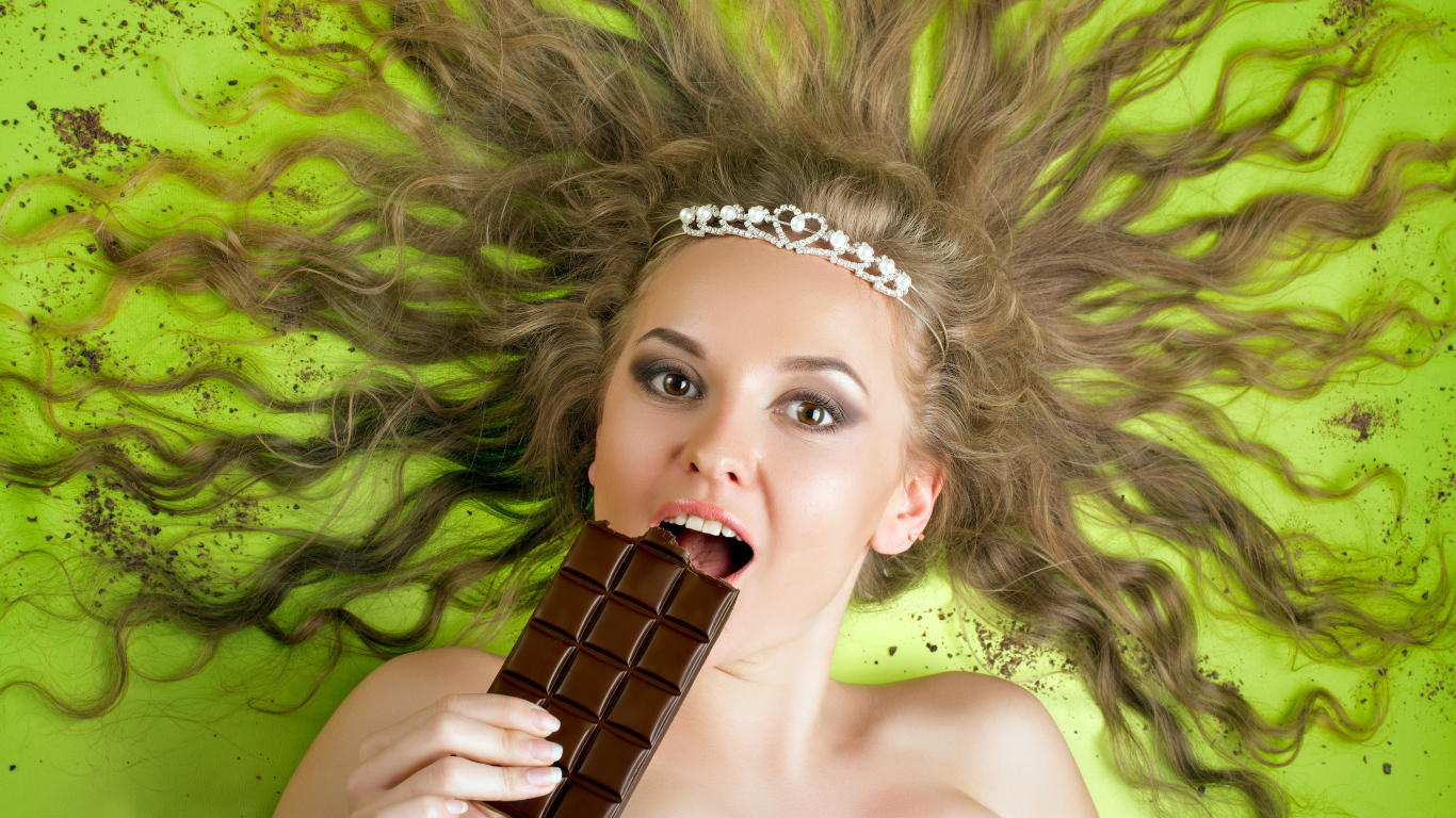 Красивая девушка с украшением в волосах лежит с шоколадкой 
