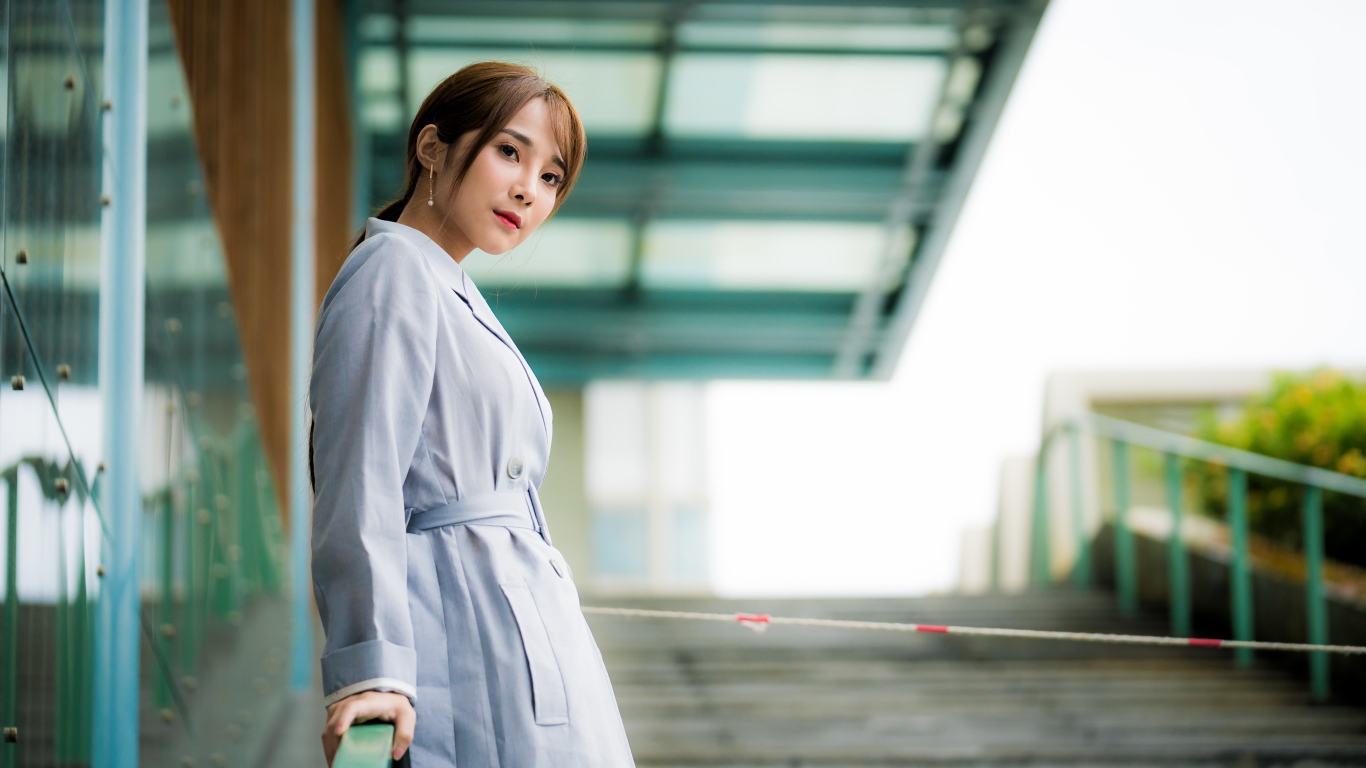 Девушка азиатка в пальто стоит у перил 