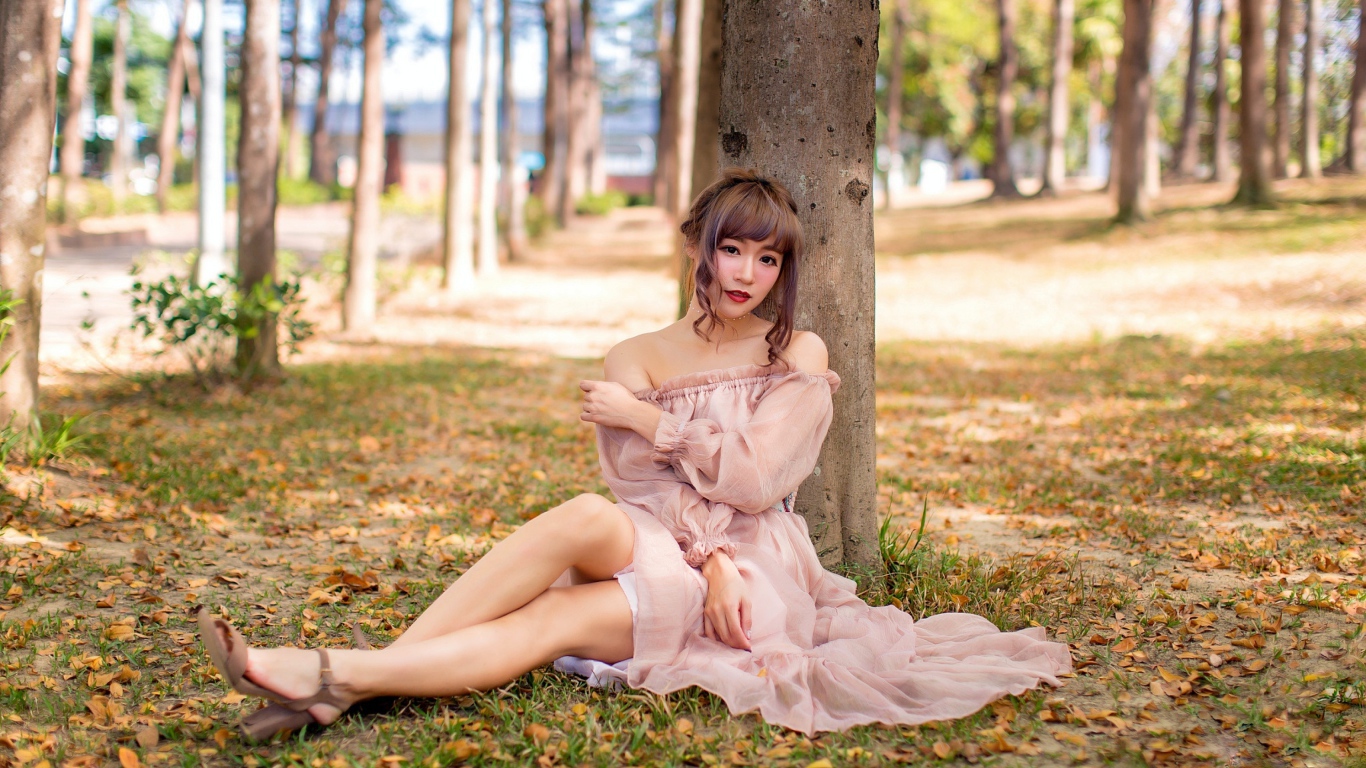 Красивая девушка азиатка в платье сидит под деревом