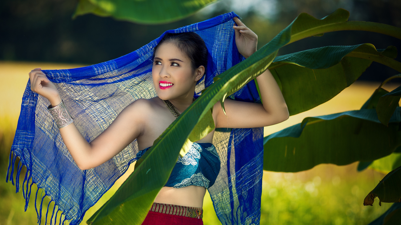 Красивая девушка азиатка с синим палантином у зеленых листьев