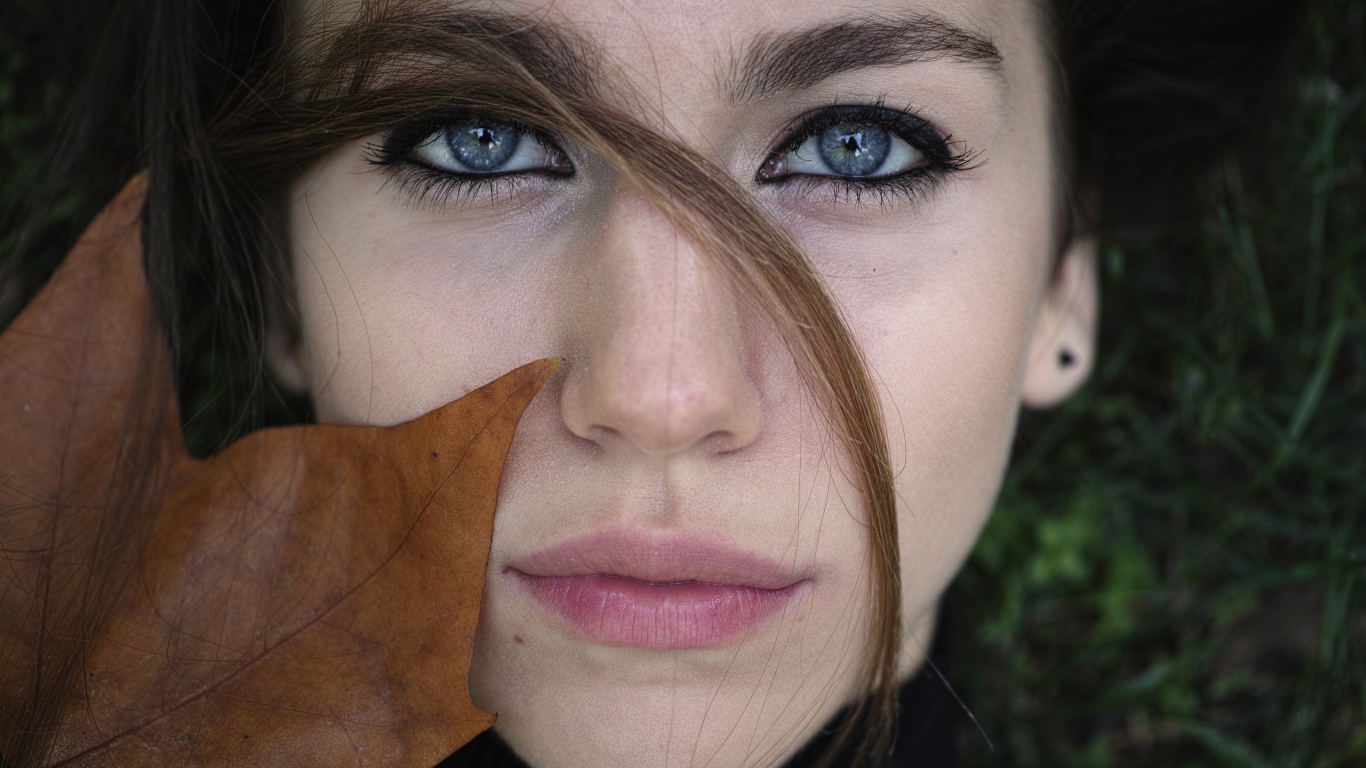 Красивая голубоглазая девушка с желтым листом у лица