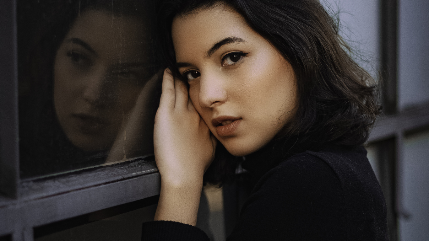 Красивая кареглазая девушка стоит у окна