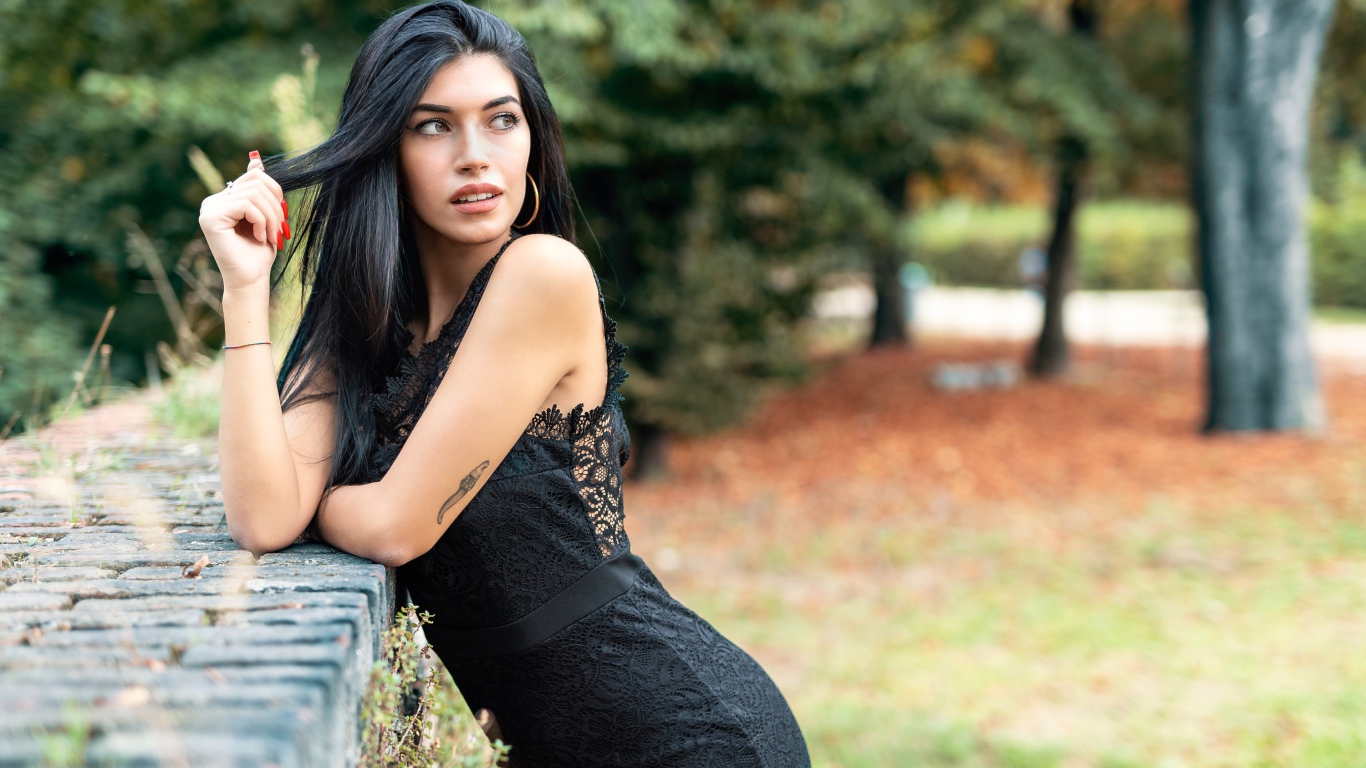 Красивая брюнетка в черном платье в парке