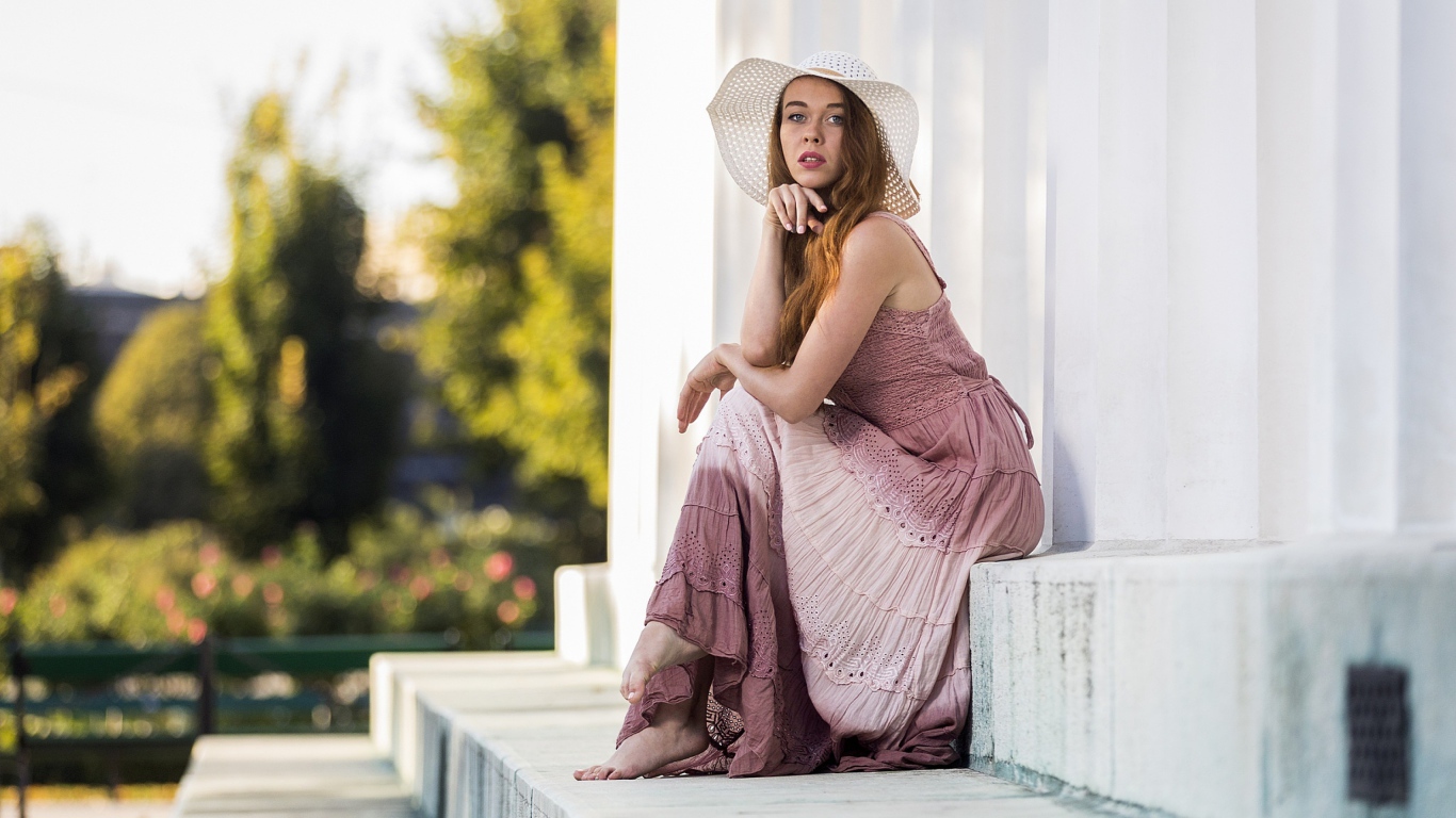 Красивая девушка в белой шляпе сидит на ступеньках 