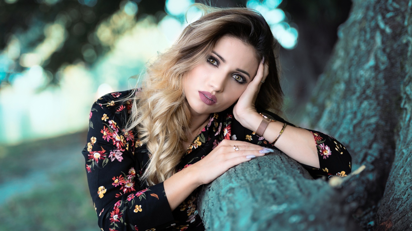 Красивая девушка в цветастом платье у дерева