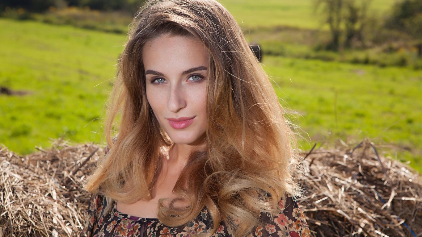 Красивая девушка с серыми глазами стоит у сена