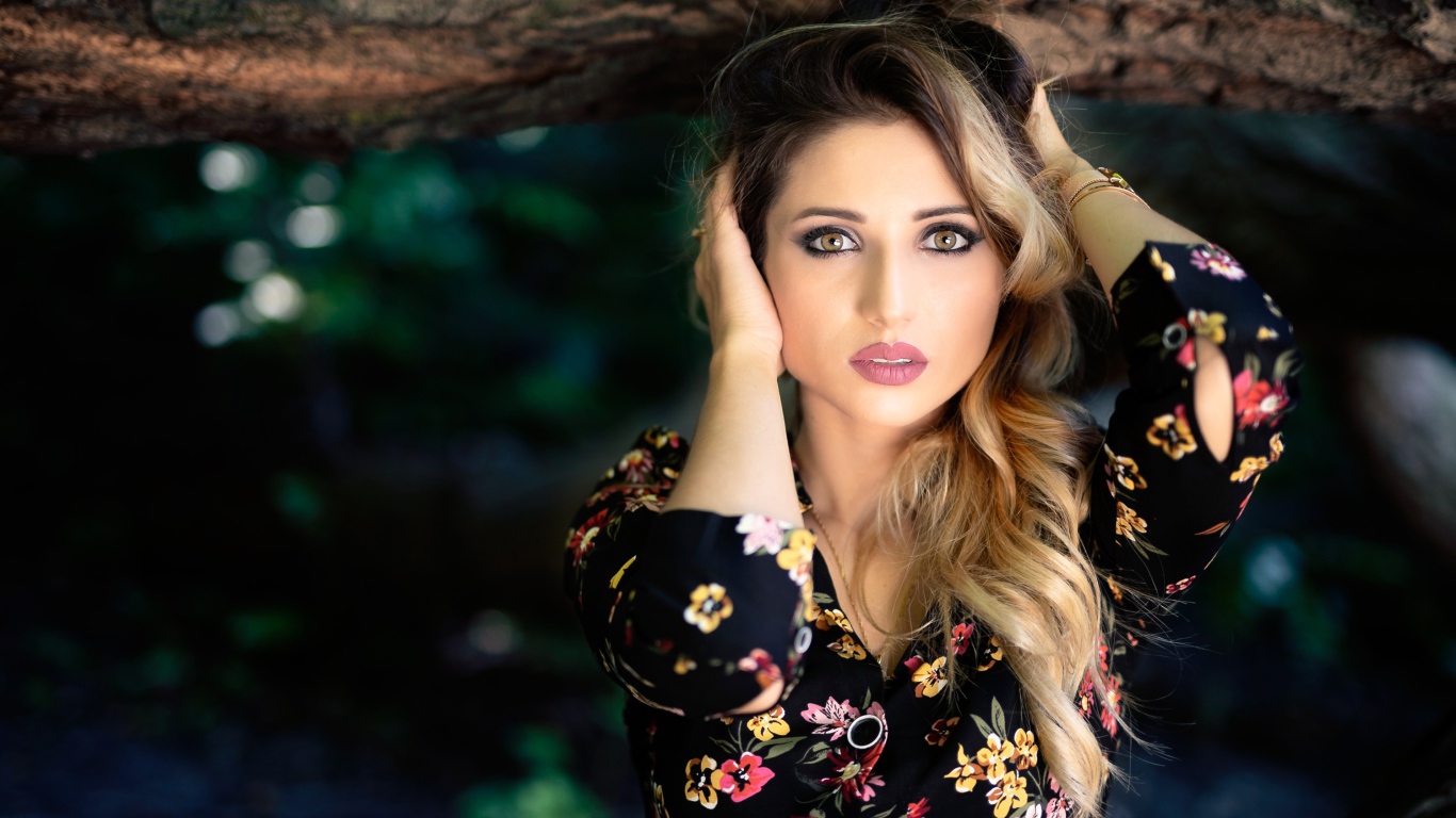 Красивая девушка с руками в волосах у дерева