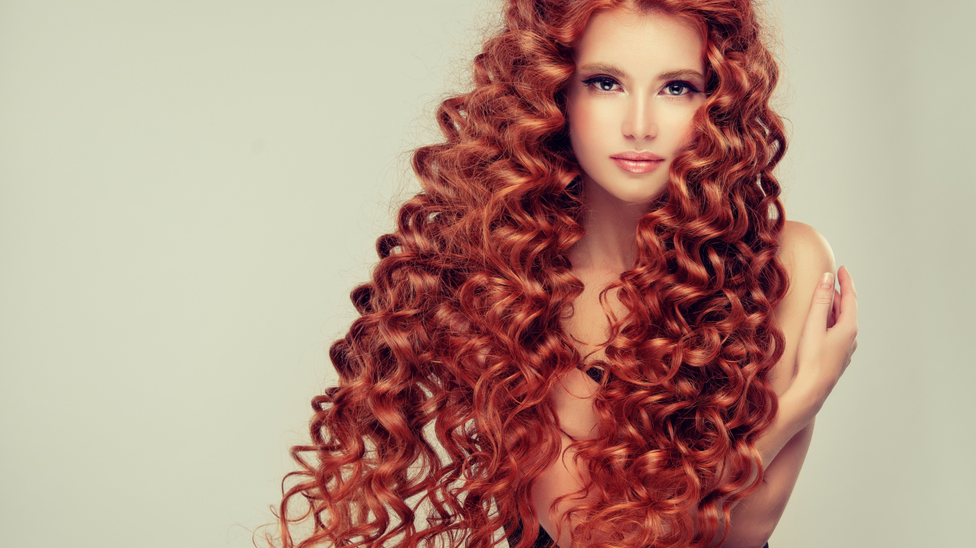 Красивая девушка с длинными рыжими волосами на сером фоне