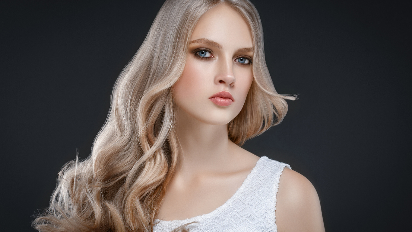 Красивая длинноволосая блондинка с голубыми глазами на сером фоне