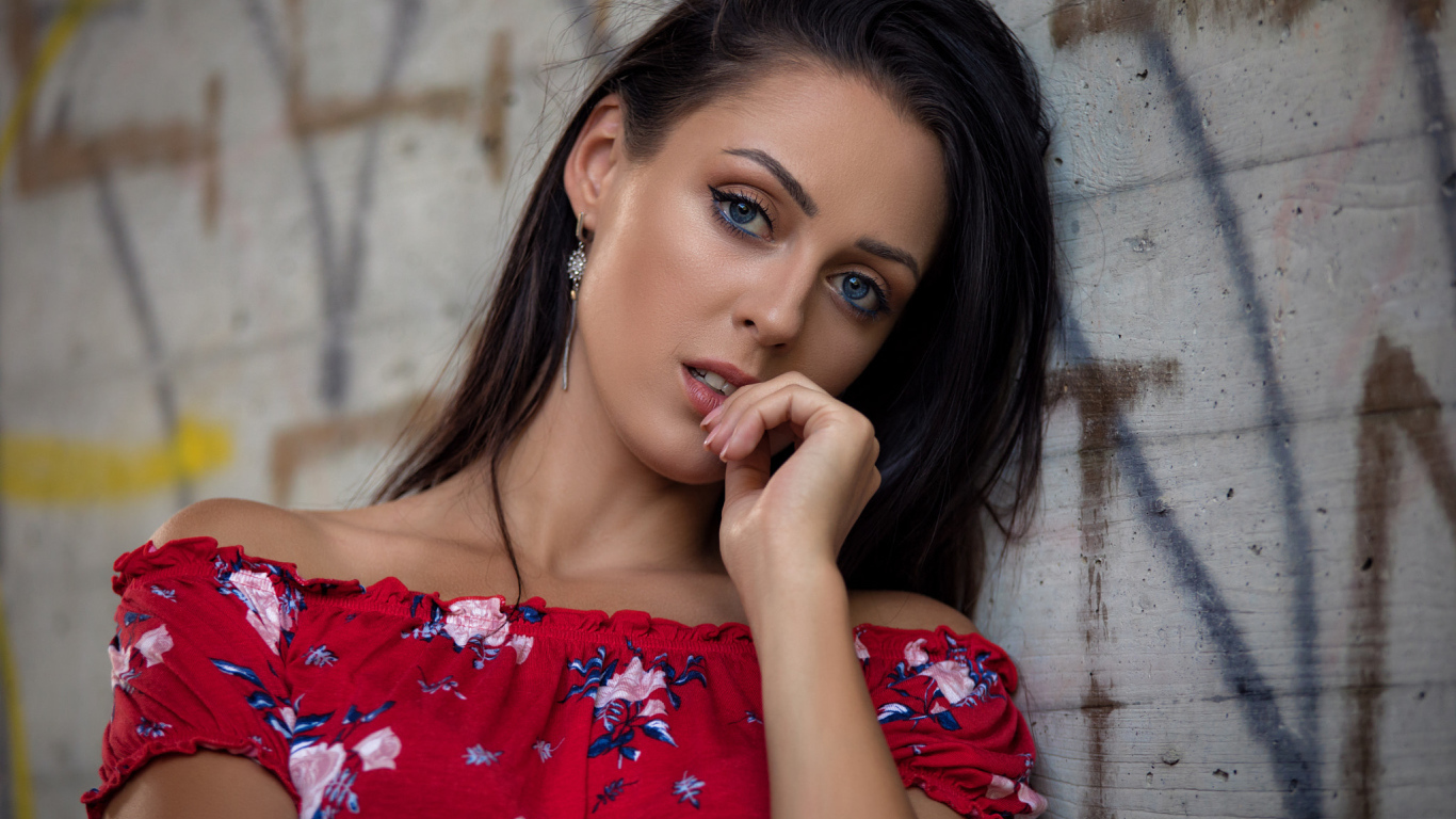 Голубоглазая брюнетка стоит в платье стоит стены