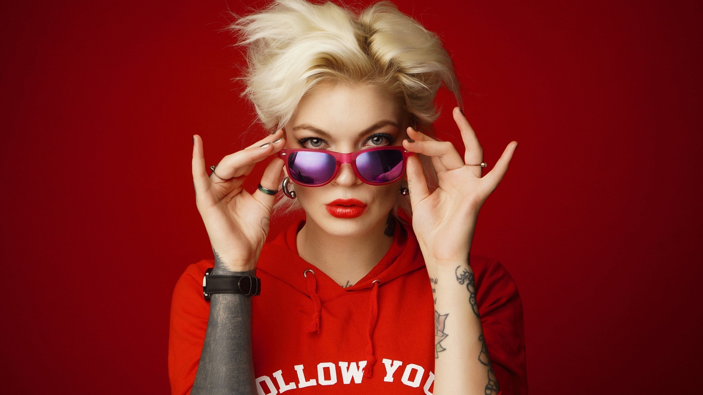 Яркая блондинка с татуировками на руках на красном фоне