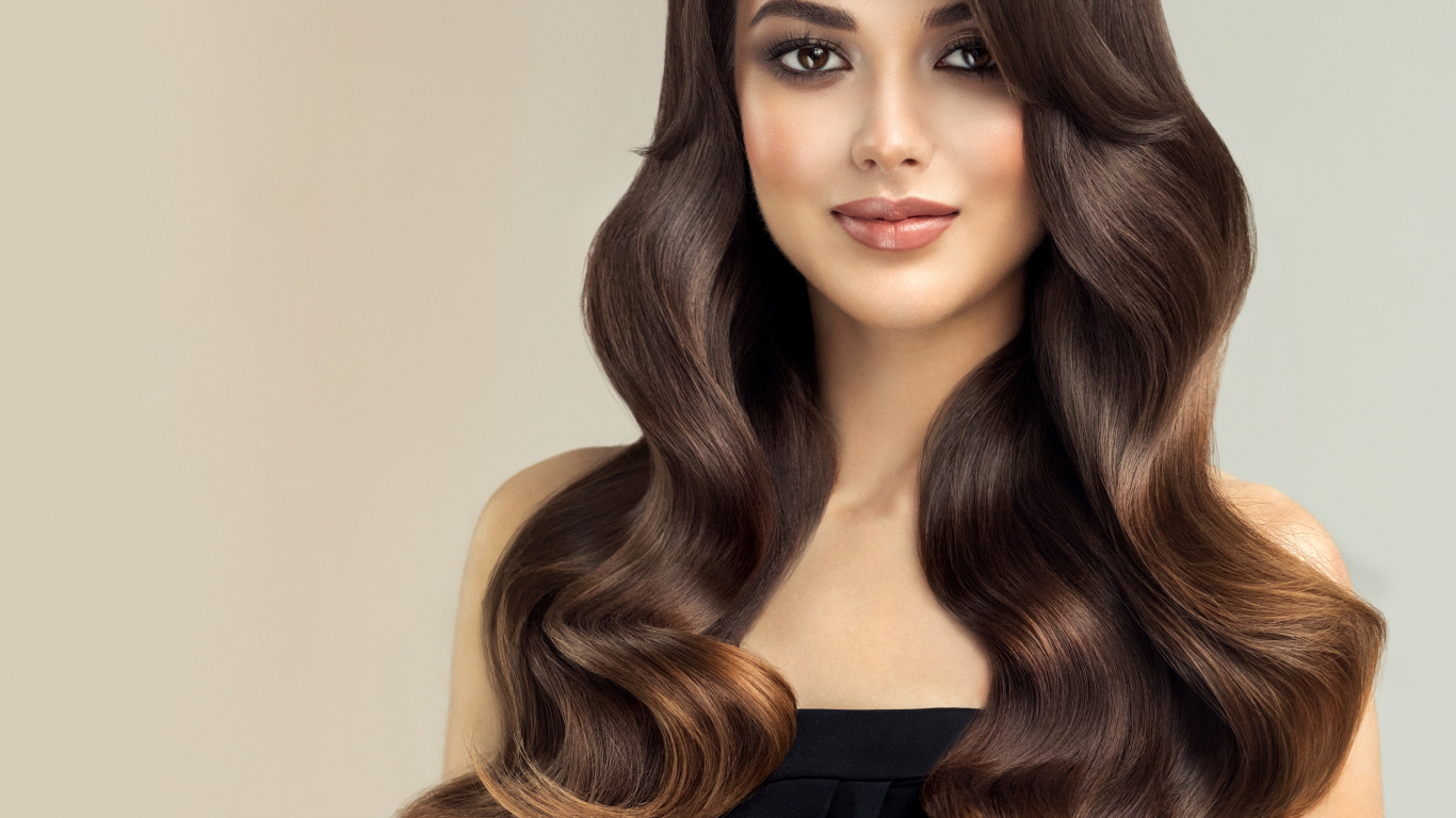 Милая кареглазая девушка с красивыми длинными волосами на сером фоне