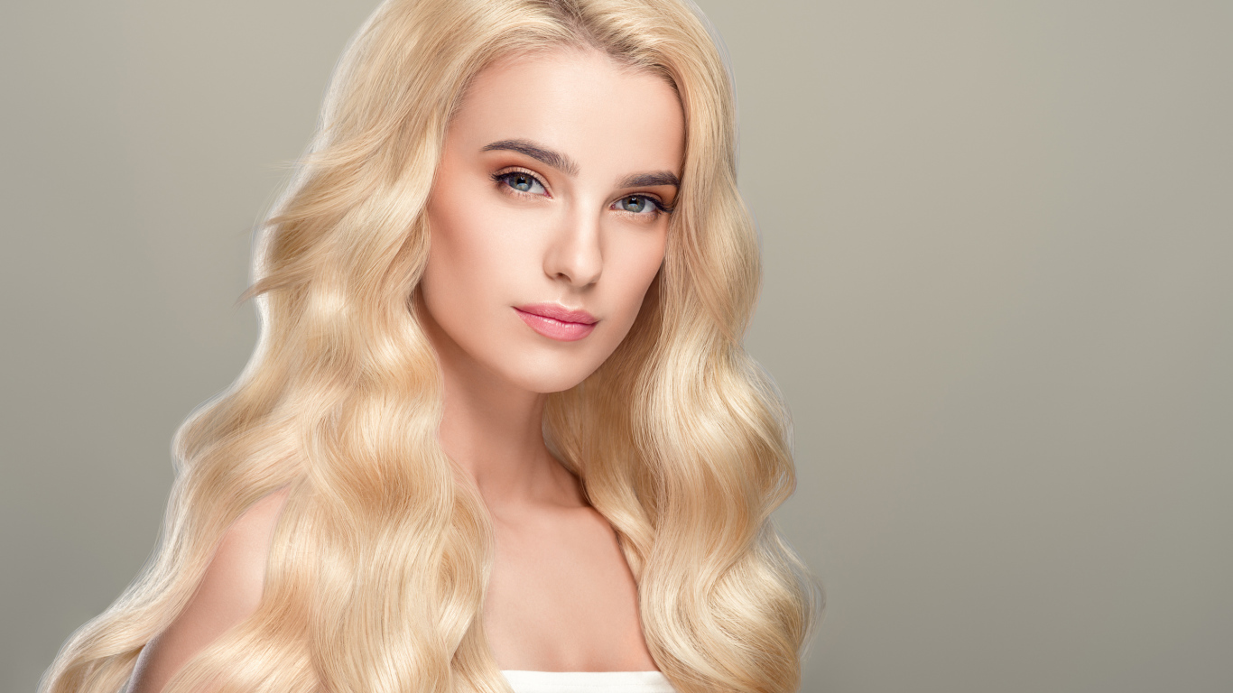 Милая длинноволосая блондинка на сером фоне