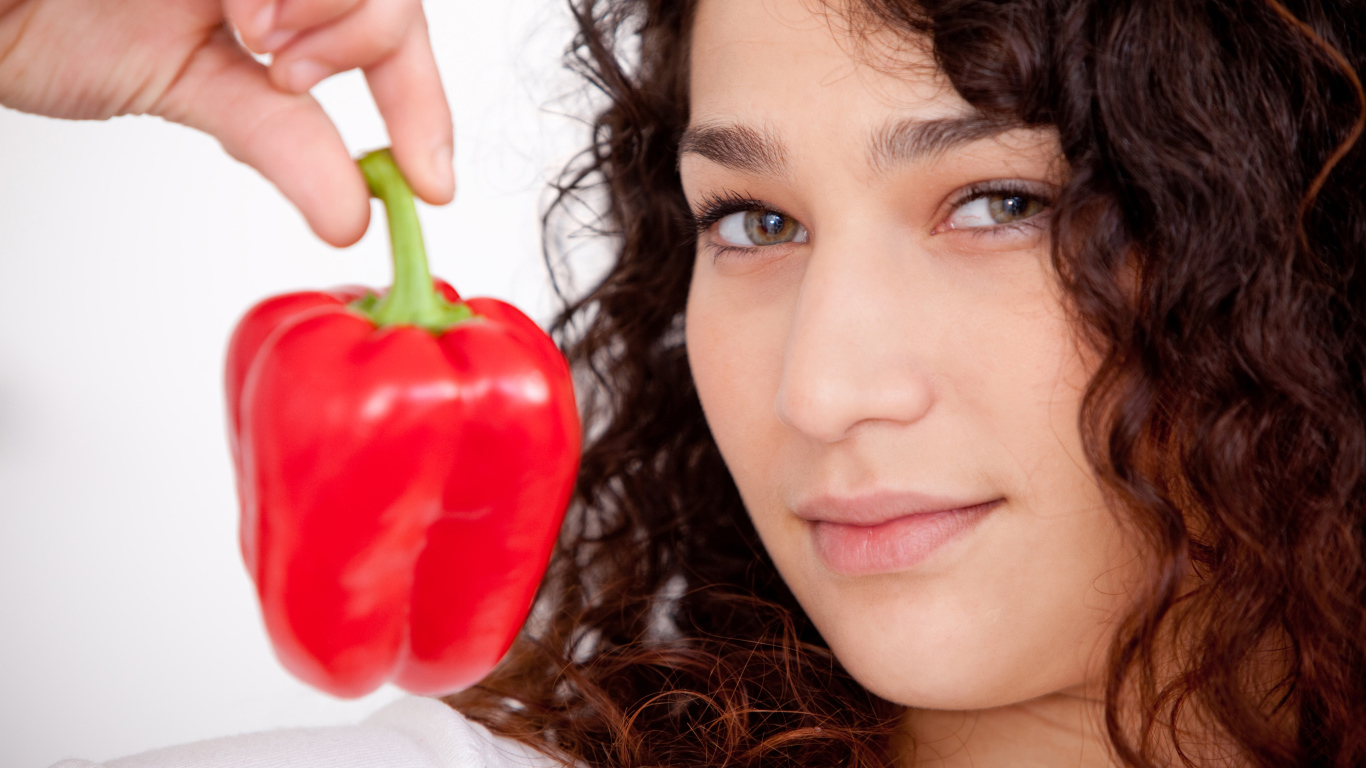 Лицо девушки с красным сладким перцем в руке крупным планом