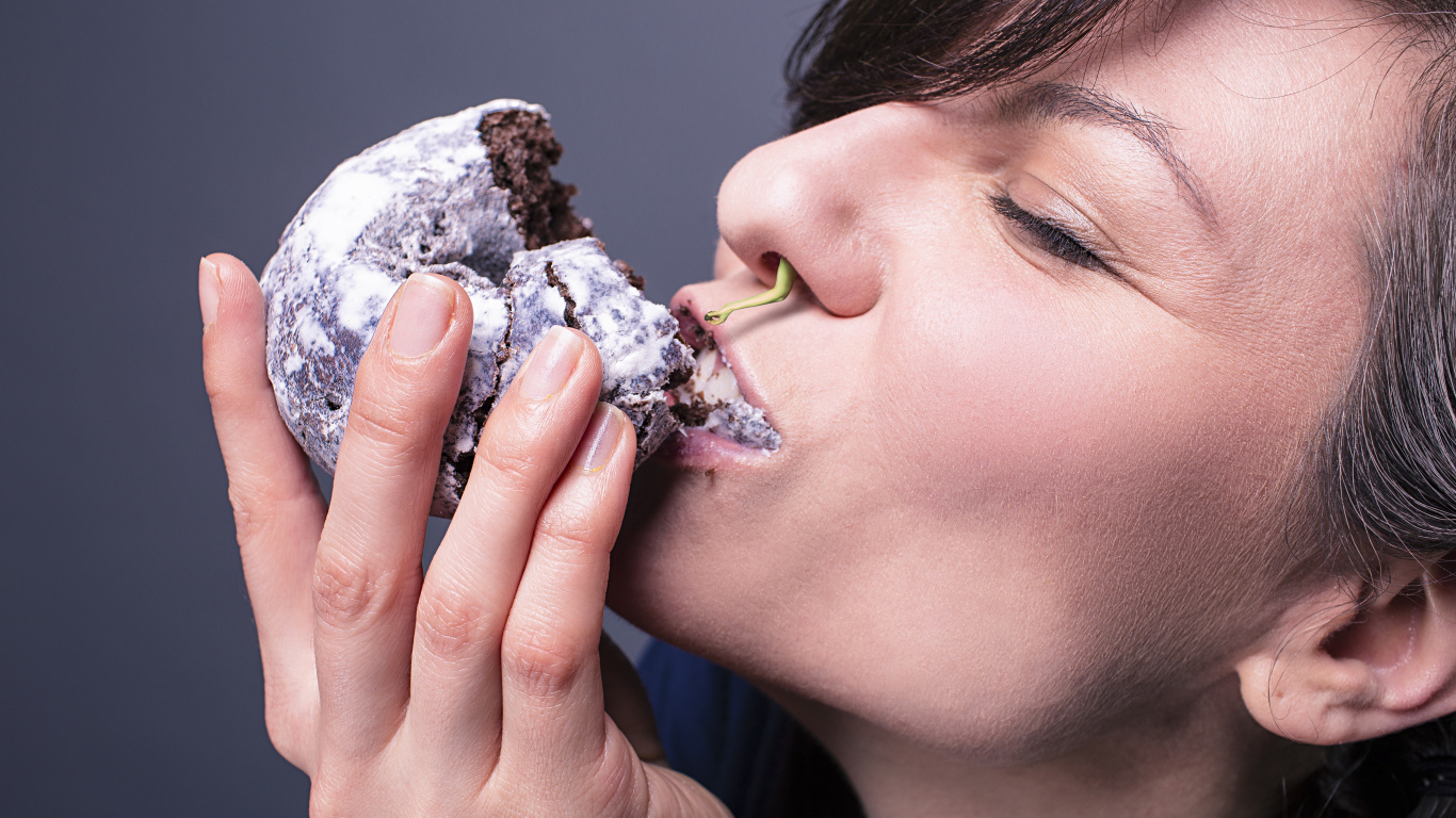 Девушка ест шоколадный пряник на сером фоне