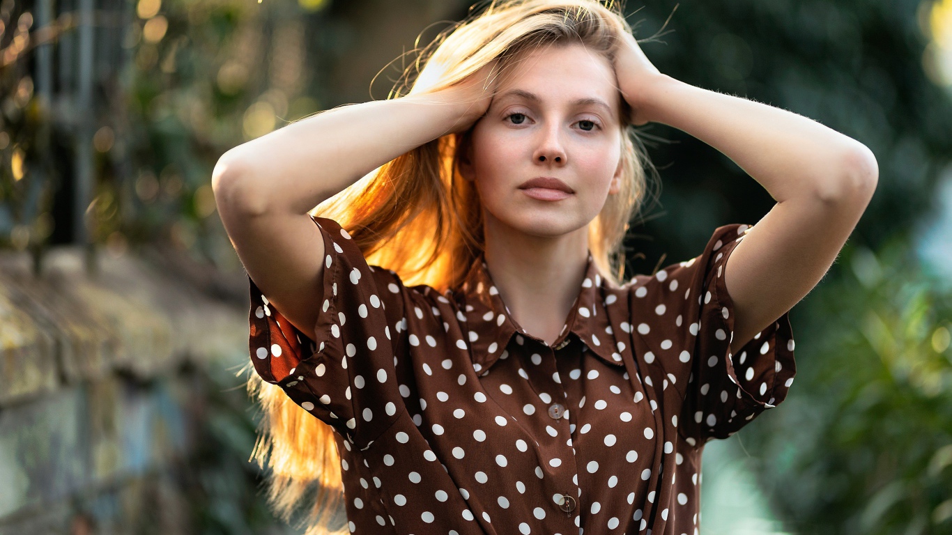 Девушка в рубашке в горох с руками в волосах 