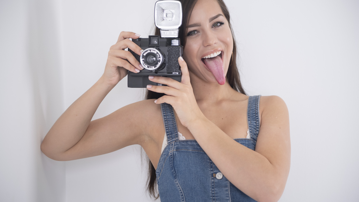Девушка с высунутым языком с фотоаппаратом в руках