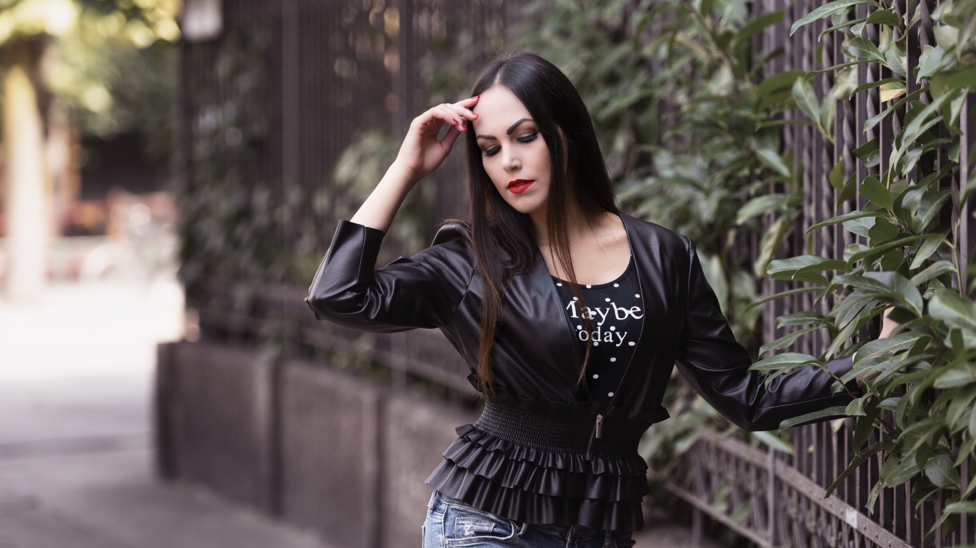 Длинноволосая брюнетка в черной куртке у забора