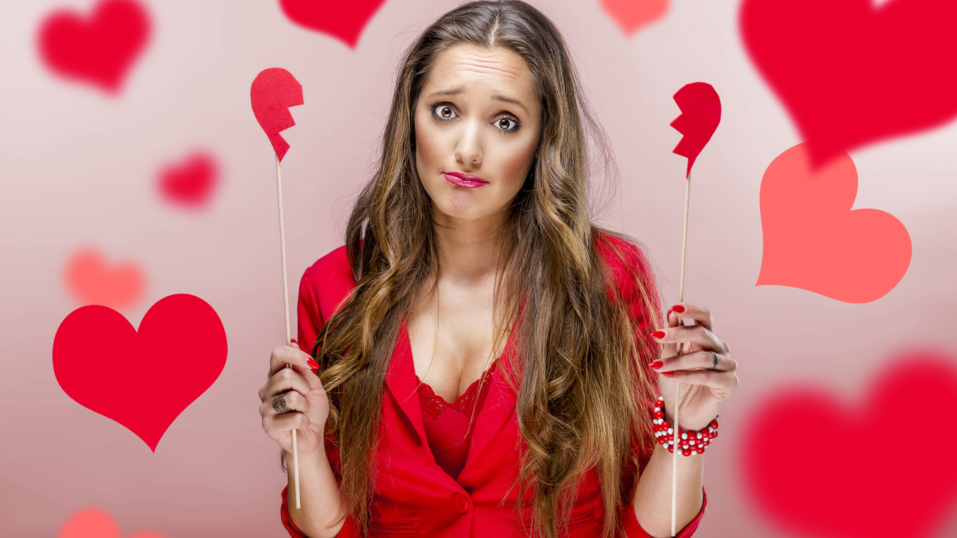 Грустная девушка с половинками бумажного сердца в руках 