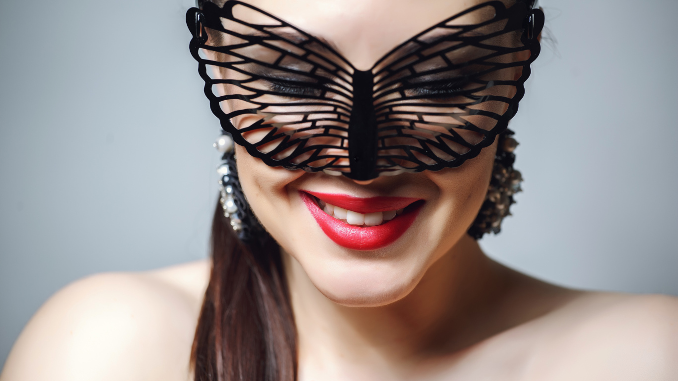 Улыбающаяся девушка в черной маске на сером фоне