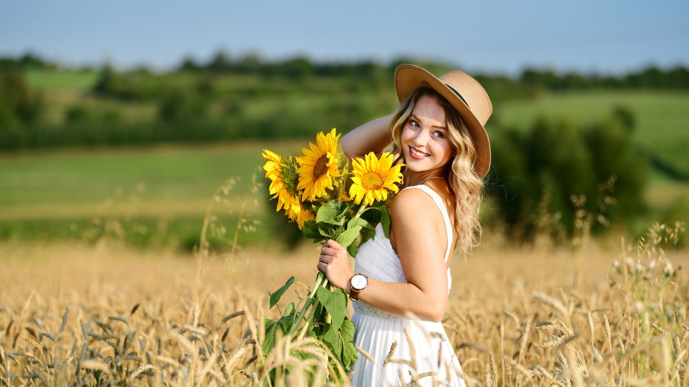 Улыбающаяся девушка на поле с пшеницей с букетом подсолнухов в руке