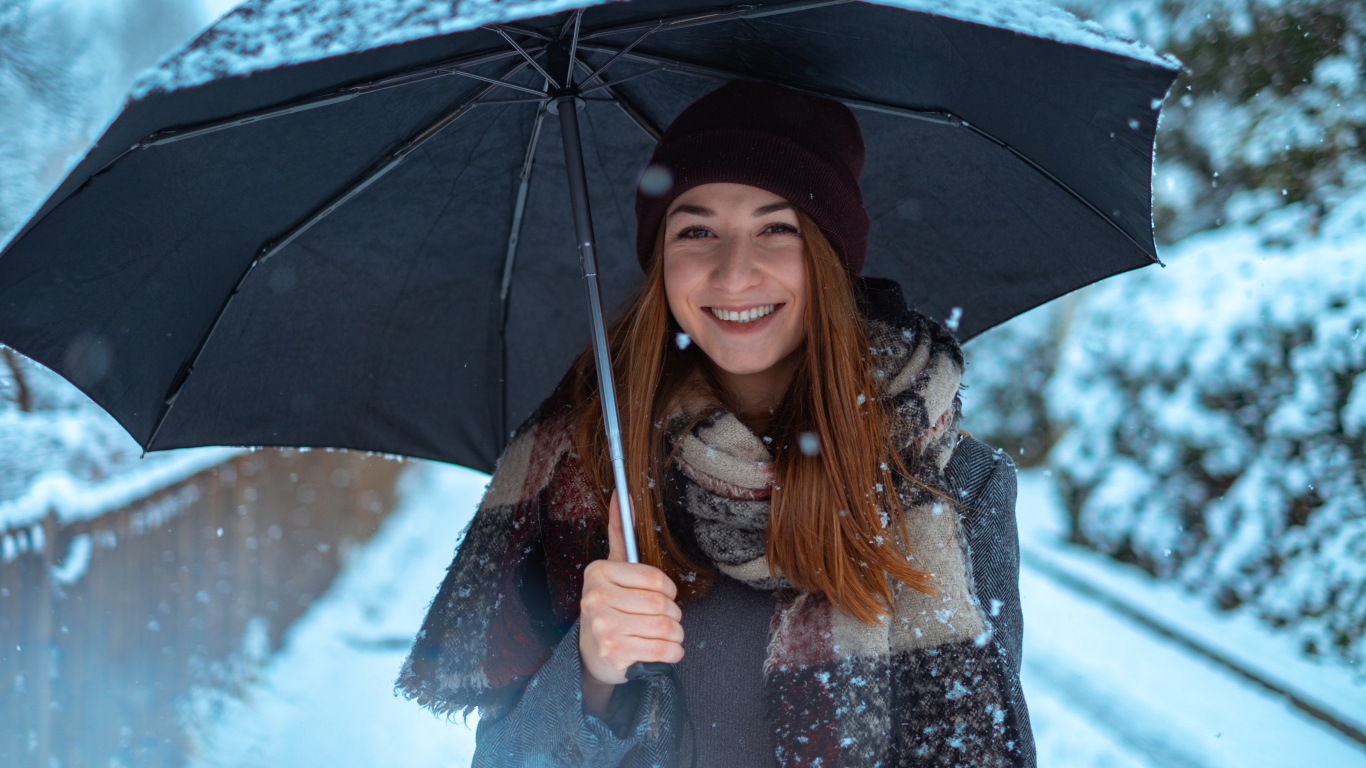 Улыбающаяся молодая девушка под зонтом зимой