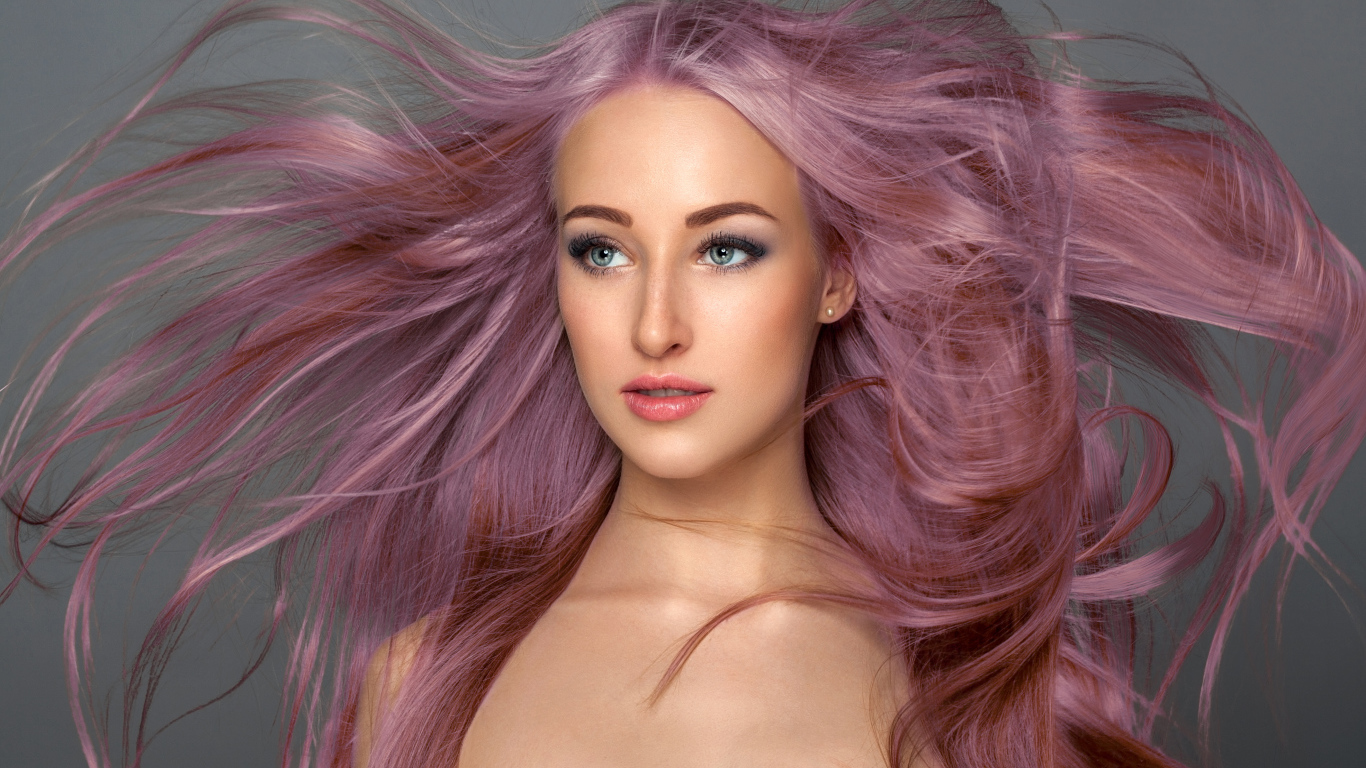 Ветер развивает розовые волосы девушки на сером фоне