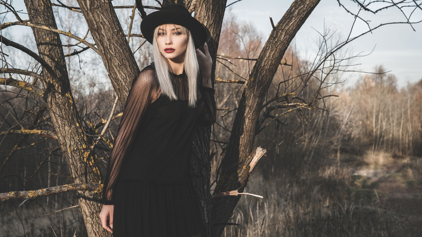 Молодая блондинка в черной шляпе у дерева