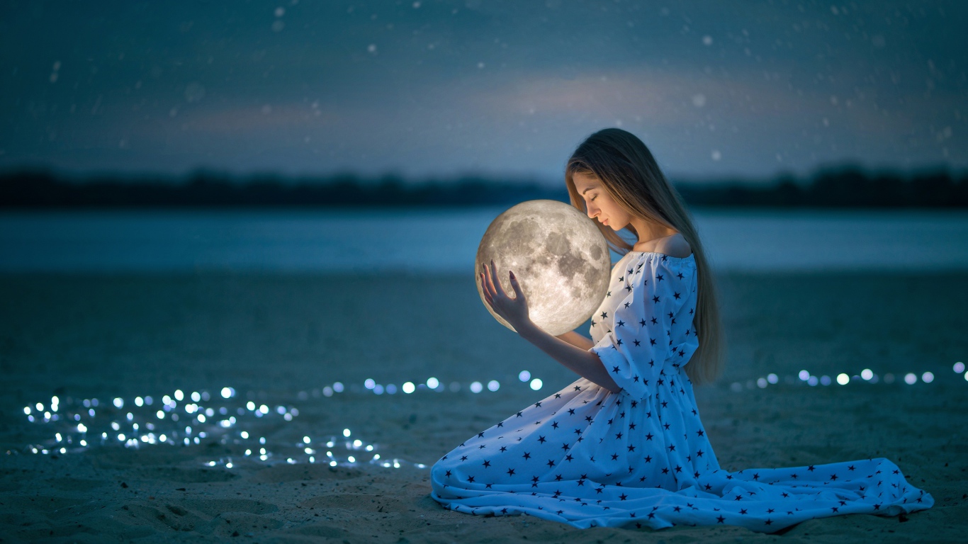 Молодая девушка в красивом платье с луной в руках на песке