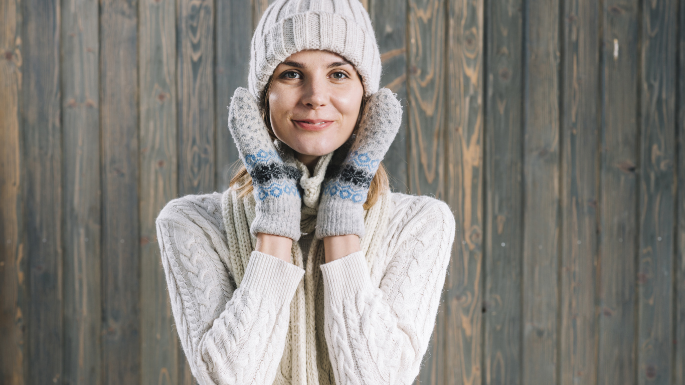 Молодая девушка на шапке, варежках  и теплой шапке на фоне забора