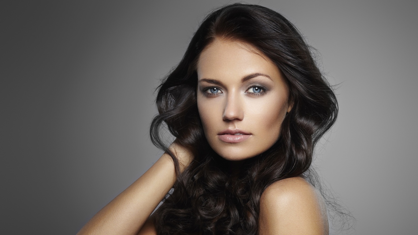 Молодая настоящая голубоглазая длинноволосая брюнетка на сером фоне