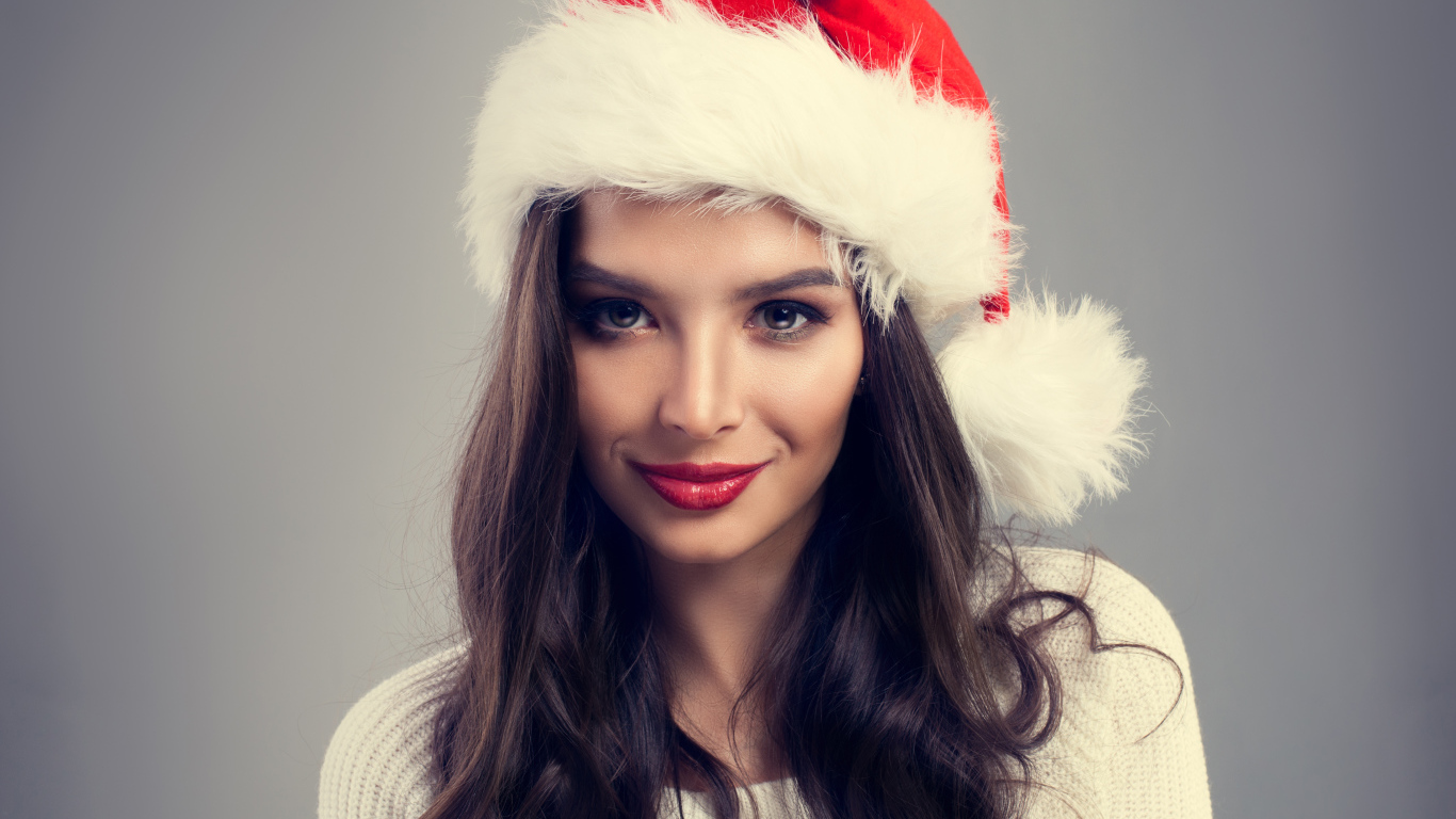 Красивая брюнетка в новогодней шапке на сером фоне
