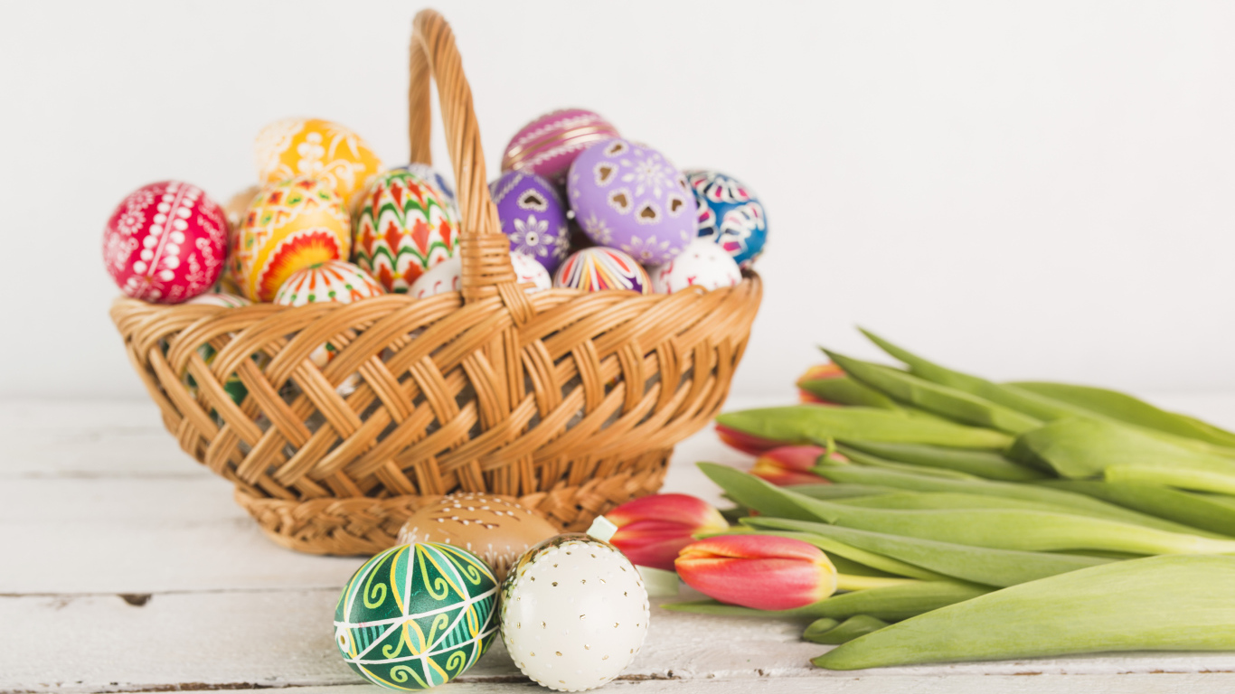 Корзина крашеных пасхальных яиц на белом фоне с букетом тюльпанов