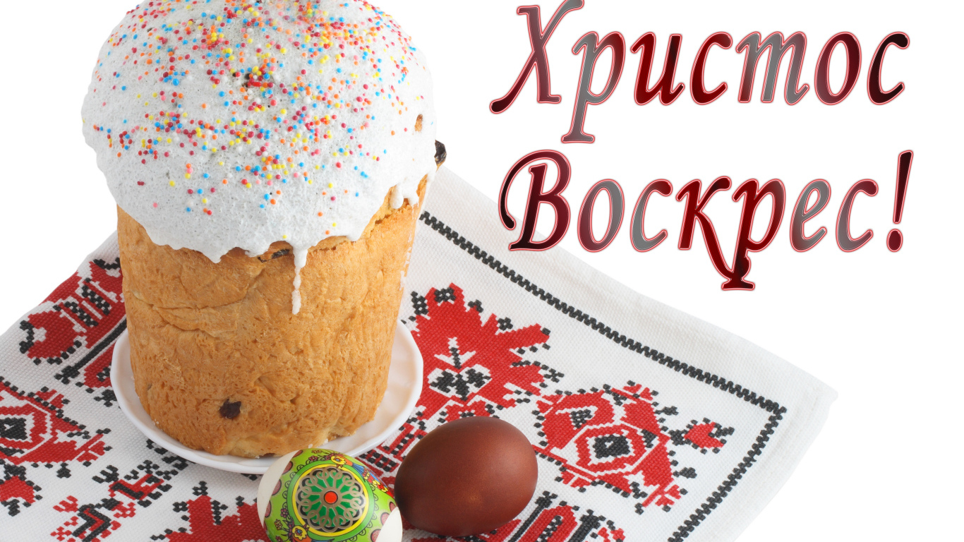 Пасхальный кулич с белой глазурью и крашеными яйцами на рушнике с надписью Христос Воскрес на белом фоне