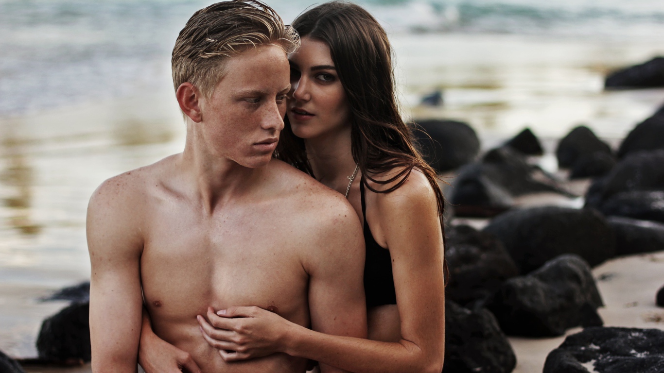 Влюбленная пара сидит на камнях на берегу моря 