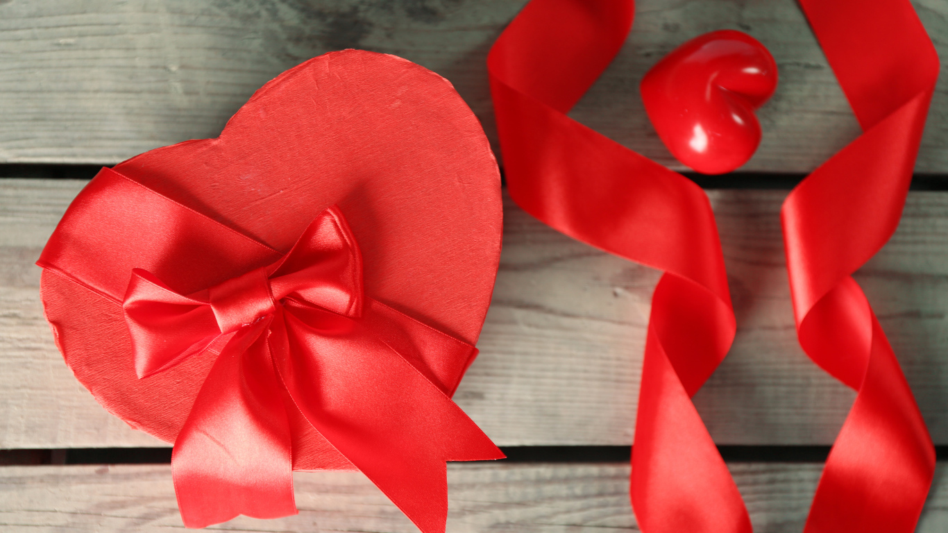 Красная коробка в форме сердца на деревянном столе с красными лентами