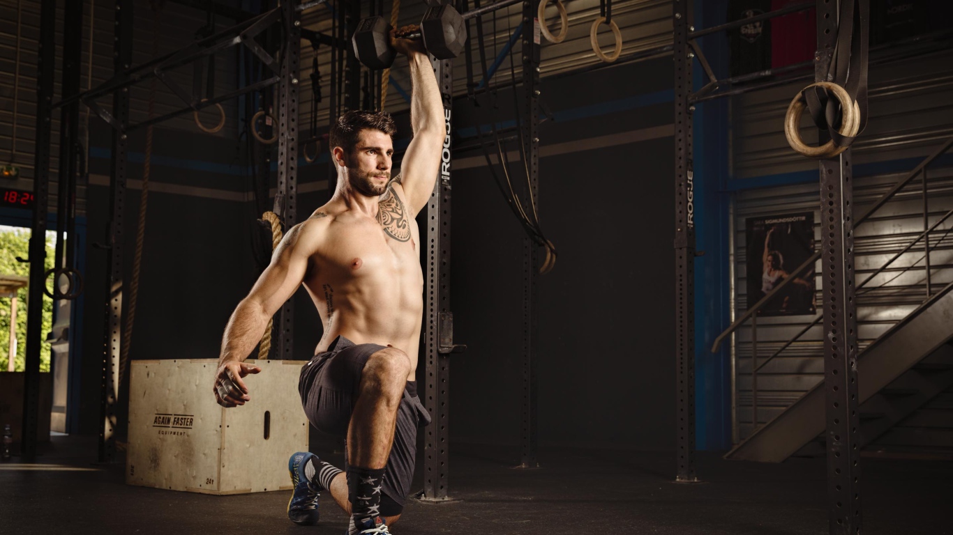 Накаченный мужчина с татуировками на теле с гантелей в руке