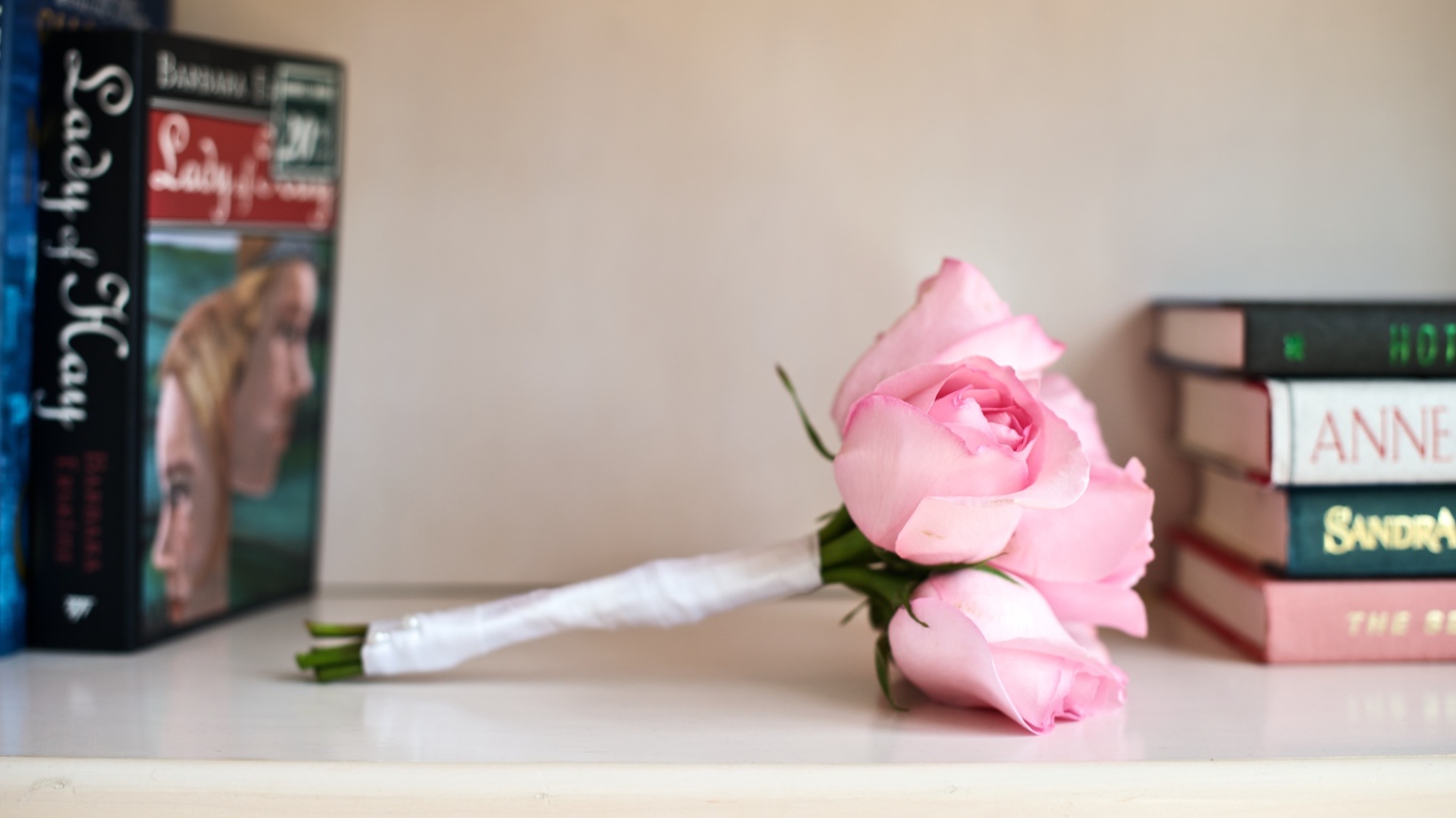 Букет розовых роз лежит на полке с книгами