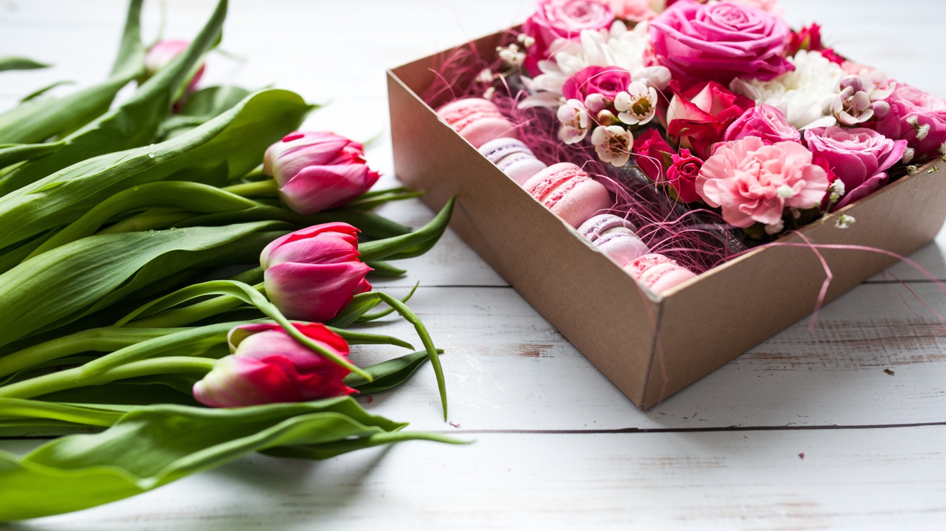 Букет розовых тюльпанов на столе с коробкой печенья макарон и цветами