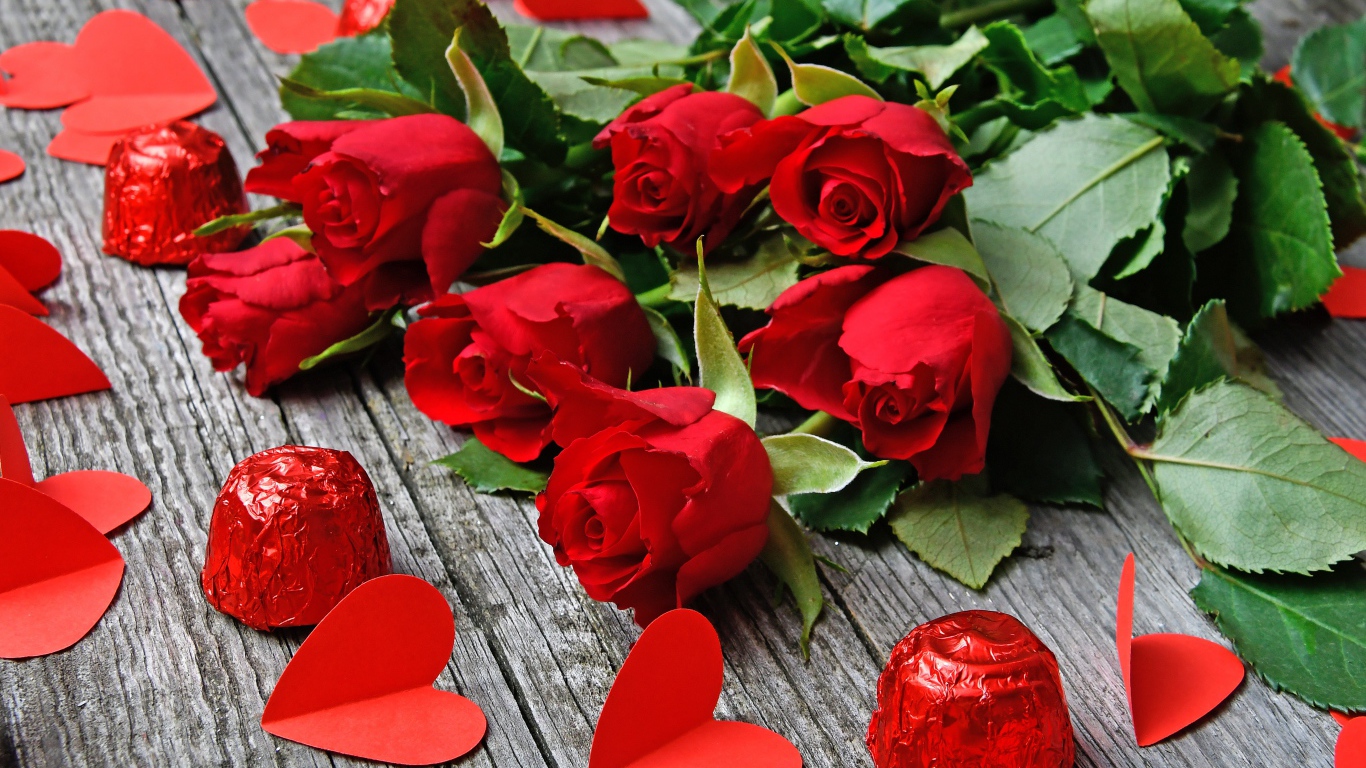 Букет красных роз на деревянном столе с конфетами и красными сердечками
