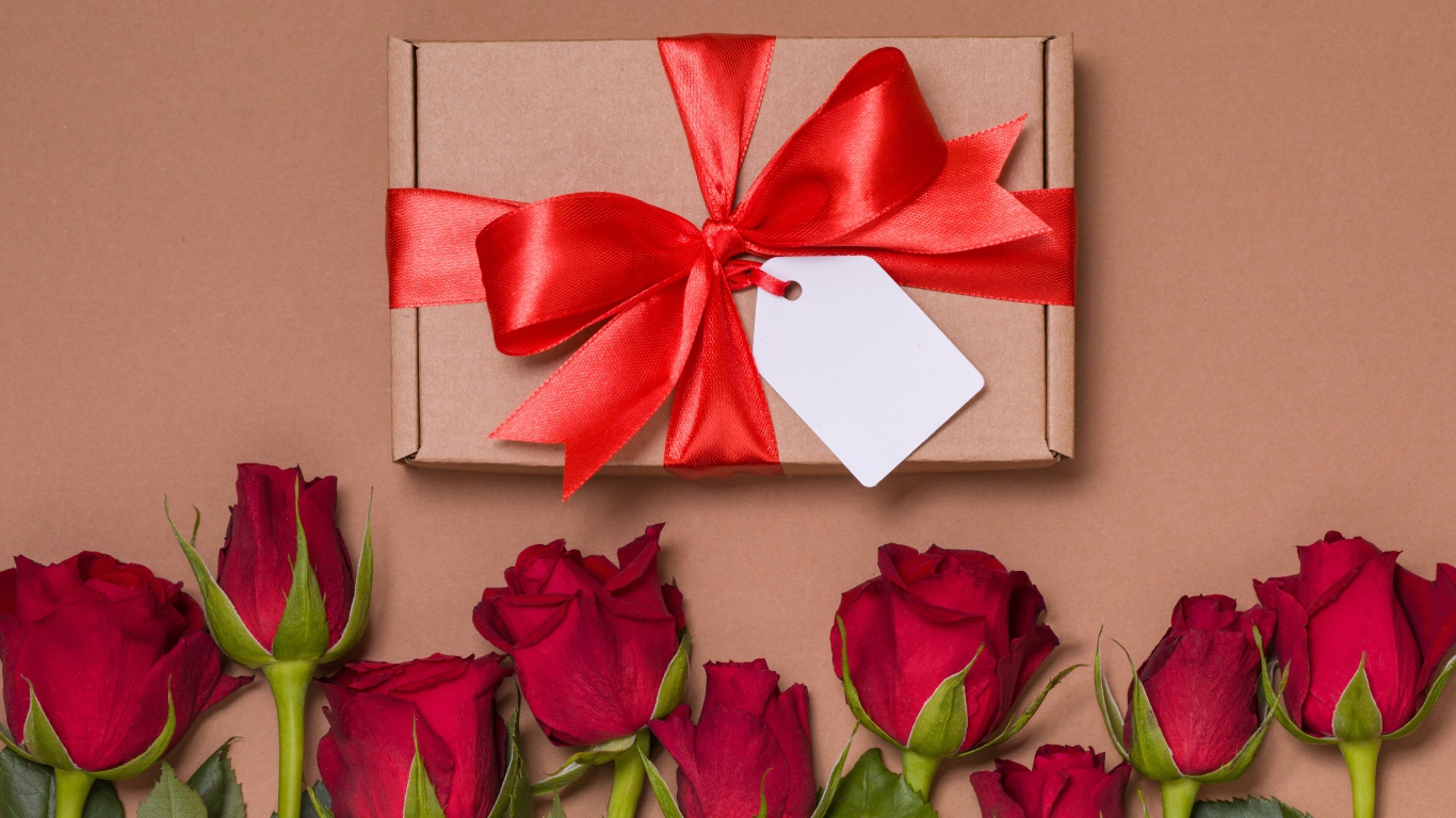 Подарок с красным бантом на бежевом фоне с красными розами