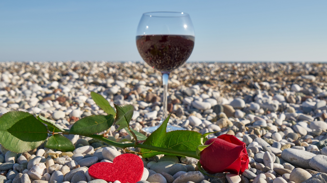 Красная роза на морской гальке с сердечком и бокалом вина