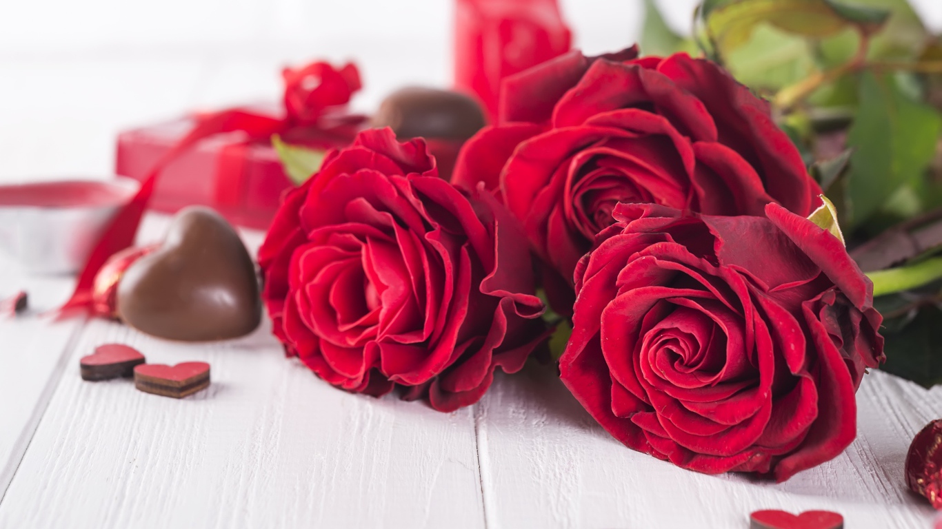 Три красивые красные розы на столе с конфетами