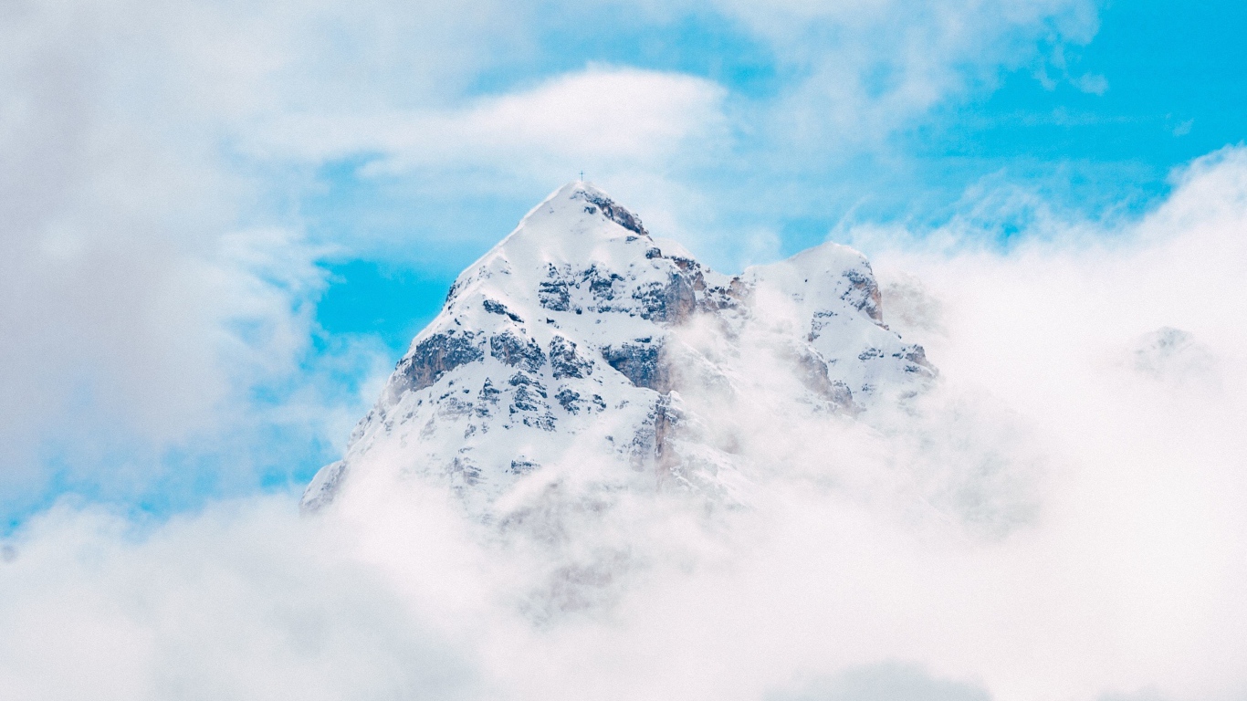 Заснеженная вершина горы в белых облаках под голубым небом