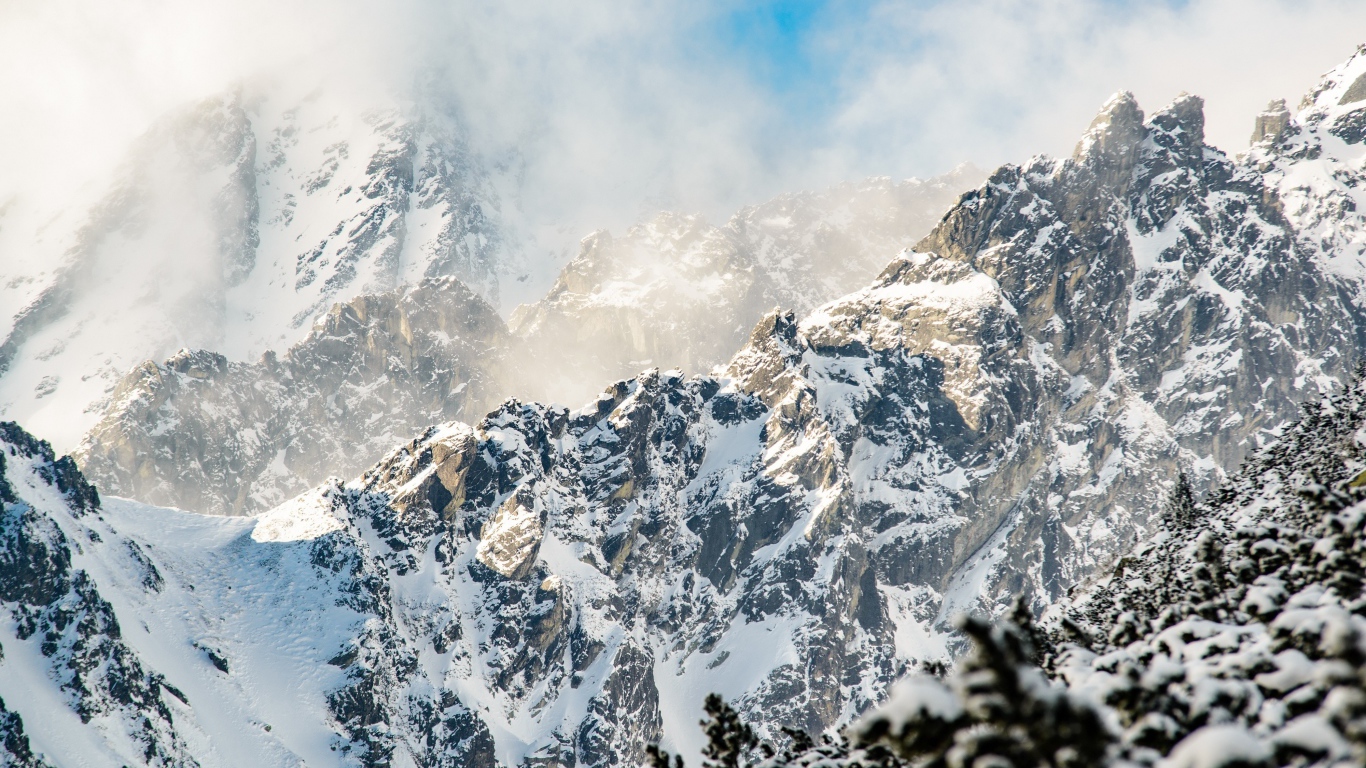 Заснеженные вершины гор под белыми облаками в голубом небе