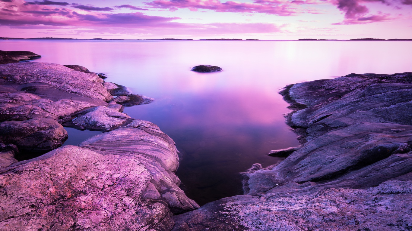 Lilac sunset in the sky over the water and stones