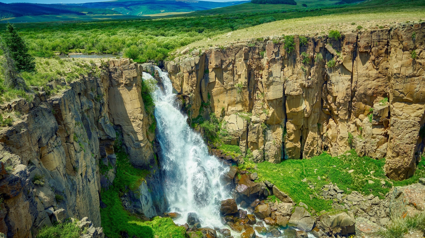 Быстрая вода водопада стекает по утесу на фоне голубого неба