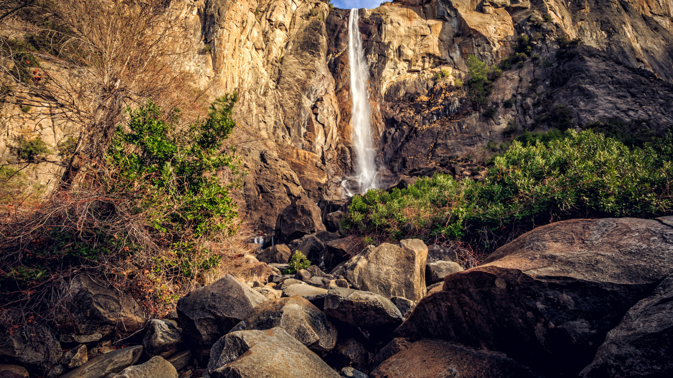 Водопад стекает с высокой скалы на камни 